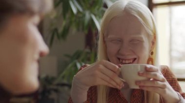 Uzun saçlı modern albino kızın en iyi arkadaşıyla kafede sohbet ederken ve cappuccino içerken seçmeli odak noktası.