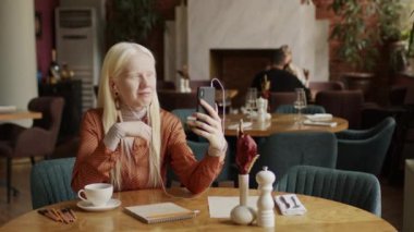 Beyaz saçlı, beyaz saçlı, restoranda oturmuş video konuşmasında sohbet eden beyaz bir kadının seçmeli odak noktası.