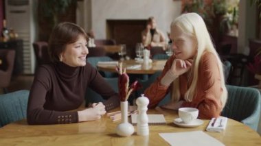 Lokantada oturmuş sohbet eden neşeli Z jenerasyonundaki iki kızın seçici odak portresi.