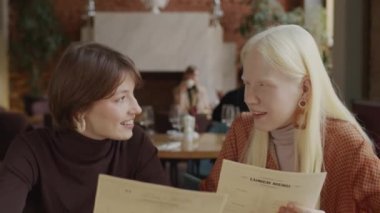 Modern restoranda yemek ve yemekleri tartışan iki neşeli genç kadının seçici odak noktası.