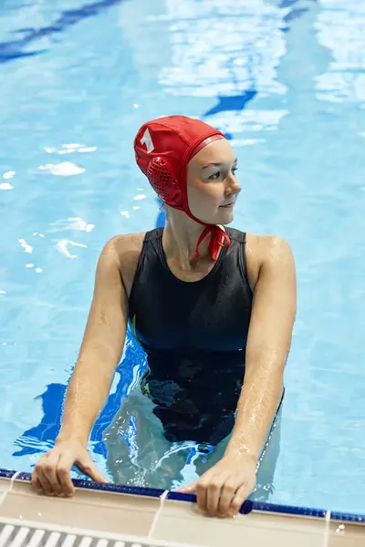 赤い水泳帽子と黒い水着の若い穏やかな女性 プールの純粋な青い水に立って ゲームの前に脇を見る — ストック写真