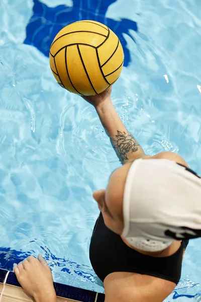 ゲーム中に純粋な青い水でプールに立っている間 黄色いボールを保持する水着の若い女性アスリートのトップビュー — ストック写真