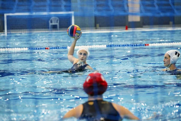 若い女性の水球選手はライバルチームのゲートにボールを投げ 水泳プールの青い水でゲーム中に防衛を見ています — ストック写真