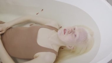 Genç albino kadının kahverengi kolsuz bluz giyip balıkla küvette dinlendiği yüksek açılı bir fotoğraf.