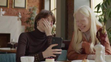 Modern restoranda birlikte vakit geçiren iki genç kızın portresi. Akıllı telefondaki komik fotoğraflara bakıp gülüyorlar.
