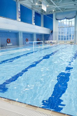 Uzun, derin ve geniş yüzme havuzunun bir parçası. Modern stadyumun içinde, spor malzemeleriyle şeffaf mavi su var.
