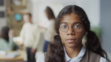 Sınıfta kameraya bakarken uzun saçlı, gözlüklü, siyah bir kızın seçici odaklı yavaş yavaş portresi.