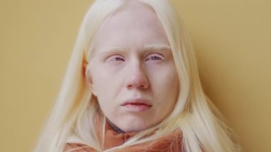 Makyajsız genç albino kadının yakın plan portresi. Kış günü kamerada sarı duvara poz veriyor.