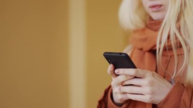 Beyaz saçlı, kalın elbiseli, caddede yürüyen ve akıllı telefondan bir şey izleyen genç bir kadının yavaş çekim çekimi.