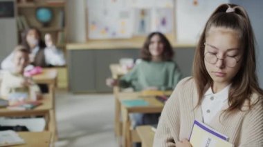 Sınıfta elinde kitaplarla duran depresif inek kızın orta sınıf odaklı portresi. Sınıf arkadaşları ona kağıt top fırlatıyor.