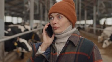 Yetişkin, beyaz bir kadının ahşap ahırda telefon görüşmesi yaparken orta boy seçici bir fotoğraf.