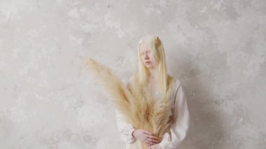 Kurumuş çiçek buketi tutan beyaz elbiseli genç albino kadının fotoğrafına zum yap ve kameraya bak.