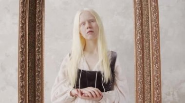 Fotoğraf çerçevesinde korse tarzı pozlar veren klasik beyaz elbiseli genç albino kadının stüdyo portresini yakınlaştır