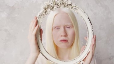 Genç albino kadının stüdyo portresi. Elinde vintage çerçeveyle kameraya bakıyor.