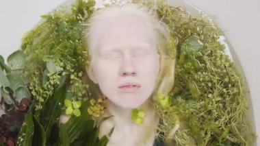 Çeşitli yeşil bitkilerle dolu küvette rahatlatıcı albinizmi olan genç bir kadının üst-alt-üst görüntüsü.