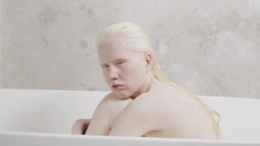 Banyo küvetinde oturmuş, dizlerine sarılıp bir şeyler düşünen endişeli genç bir kadının portresi.