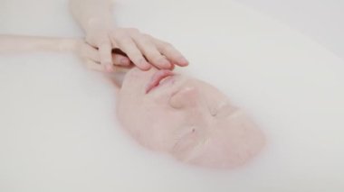 Genç albino kadının yakın plan portresi süt banyosunun keyfini çıkarırken nazikçe cildini okşuyor.
