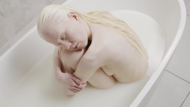 裸女白化病患者高角肖像 双目紧闭在充满牛奶的浴缸里 抱着她的膝盖 — 图库视频影像
