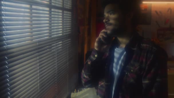 中肖像画的年轻中东男人站在车库里的窗前打电话 透过百叶窗凝视 90年代的美学 — 图库视频影像