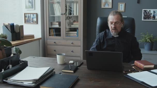 现代成熟的高加索天主教牧师坐在办公室的桌旁 在视频会议上与同事们讨论一些事情 — 图库视频影像