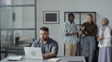 Orta Doğulu bir adamın ofiste dizüstü bilgisayarla çalışırken çekilmiş seçmeli bir fotoğrafı. İş arkadaşlarının itibarını zedelemeye çalışmasından kaçınıyor.