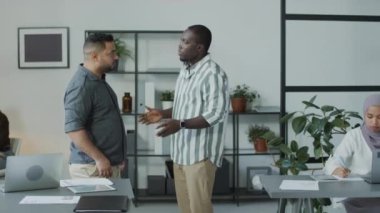 Afrika kökenli Amerikalı ve Orta Doğulu erkek meslektaşların ofiste kavgaya tutuşmalarının orta uzunlukta bir görüntüsü.