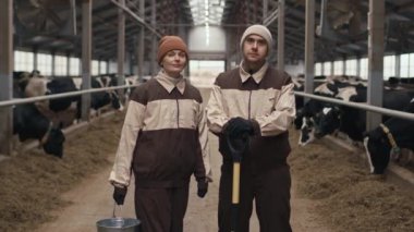 İnek ahırında dikilip kameraya bakan güveni tam bir erkek ve kadın portresi.