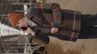 Yetişkin, beyaz bir çiftlik sahibinin inek ahırında telefonla konuşurken dikey görüntüsü.