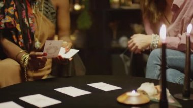 Kadın müşterinin geleceğini tahmin ederken tarot kartları okurken çekilen görüntüler stüdyoda koyu renklerde oturuyor.