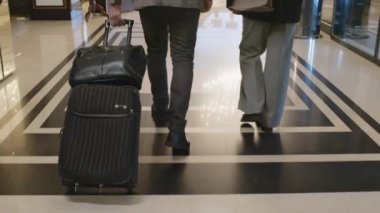 Otel lobisine bavulla giren ve resepsiyona giden misafirlerin arka görüntüsü.
