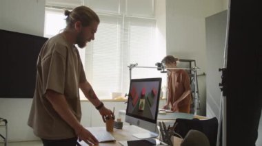 Kadın fotoğrafçının geometrik şekilleri ve küpleri yatay rafta kamerayla çekerken orta boy görüntüsü ve bilgisayar ekranında sonuca bakan erkek meslektaşı.