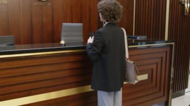 Bayan misafirin otel resepsiyonunda yöneticiyle tanışmasını ve giriş yapmasını çek.