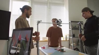 İki erkek meslektaşın teleskopik rafa monte edilmiş kamerayı kaldırmasına yardım ederken geometrik şekilli düz kompozisyon çekimleri için hazırlanırken orta ölçekli bir fotoğraf.