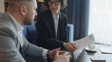 Otel odasında otururken şirket göstergelerini tartışan iş arkadaşlarının görüntülerini yukarı kaldır.