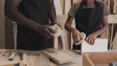 Afrika kökenli Amerikalı yetişkin ve çocuğun stüdyoda el işi yaparken tahta yüzeyini düzleştirirken çekilmiş.