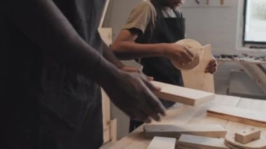 Afro-Amerikalı baba ve oğul marangozluk stüdyosunda masanın yanında yan yana dururken ahşap bir kalasla çalışıyorlar.