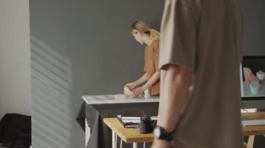 Orta boy gülümseyen beyaz kadın iş kadını ya da blogcu el yapımı kozmetik kavanozlarını masaya yerleştirirken, erkek fotoğrafçı DSR kamerasını alır ve promosyon fotoğrafları çeker.