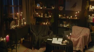 Kahin stüdyosunun yüksek açılı görüntüsü koyu renkli yanan mumlar ve müşterilerin servis alanı, masa üzerinde tarot düzeni