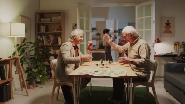 家庭で集まるときの良いチェスゲームのために互いに感謝する笑顔の年金受給者の中長いショット 背景にワインを持つ女性 — ストック動画