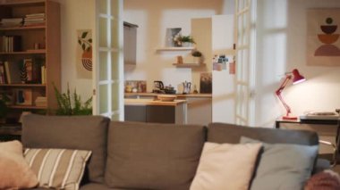 Büyük bir kanepe, gardırop, oturma odasında bitki ve arka planda küçük bir mutfak.