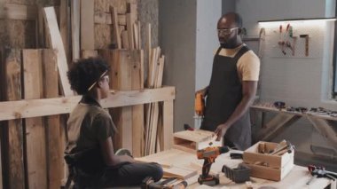 Afrikalı Amerikalı baba, marangozluk atölyesinde çalışırken oğluna çivi çakmayı öğretiyor.
