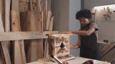 Afro-Amerikan çocuk marangozluk stüdyosundaki ahşap kuş evini cilalıyor ve siliyor.
