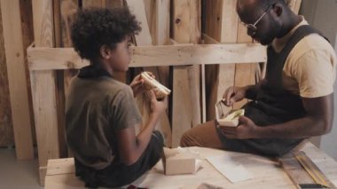 Orta boy Afrikalı Amerikalı oğul ve baba marangozluk atölyesinde dinlenirken beslenme çantasından sandviç yerken.