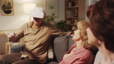 VR gözlükleri üzerinde arkadaşlarıyla rahat oturma odasında vakit geçirirken emeklinin uzaktan kumanda modu değiştirdiği orta boy bir kare.