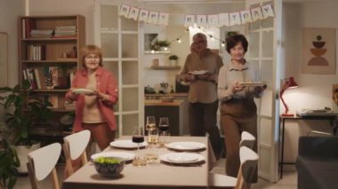 Neşeli yetişkinlerden oluşan küçük bir grup salata ve atıştırmalıkları festival masasına koyup doğum günü partisinde yemek yemeye hazırlanıyor.