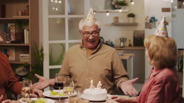 居心地の良いパーティーで友達と65周年を祝うときにケーキにろうそくを吹き飛ばすポジティブな高齢者の中型ショット — ストック動画