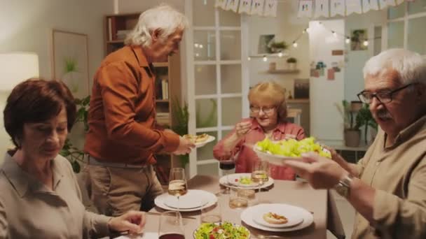在舒适的家庭生日庆祝会上 一对年长的夫妇坐在餐桌旁 用喜庆的菜式招待朋友 — 图库视频影像
