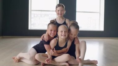 Beyaz giysili küçük beyaz jimnastikçilerin portresi. Yerde oturup kameraya bakarken birbirlerine sarılıyorlar.