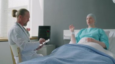 Genç kadın onkoloji hastasının yatakta yatarken sağlık durumuyla ilgili doktorla konuştuğu orta boy bir fotoğraf.