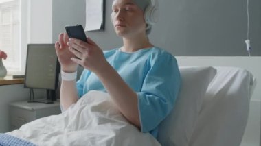 Kadın onkoloji hastasının hastane koğuşunda yatarken ve iyileşme sürecindeyken cep telefonu kullanmasını çek.